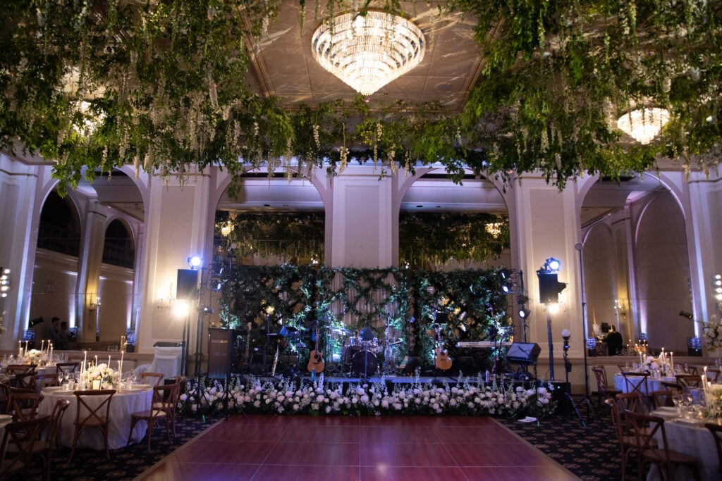 Wedding band stage surrounded by white flowers and hanging greenery