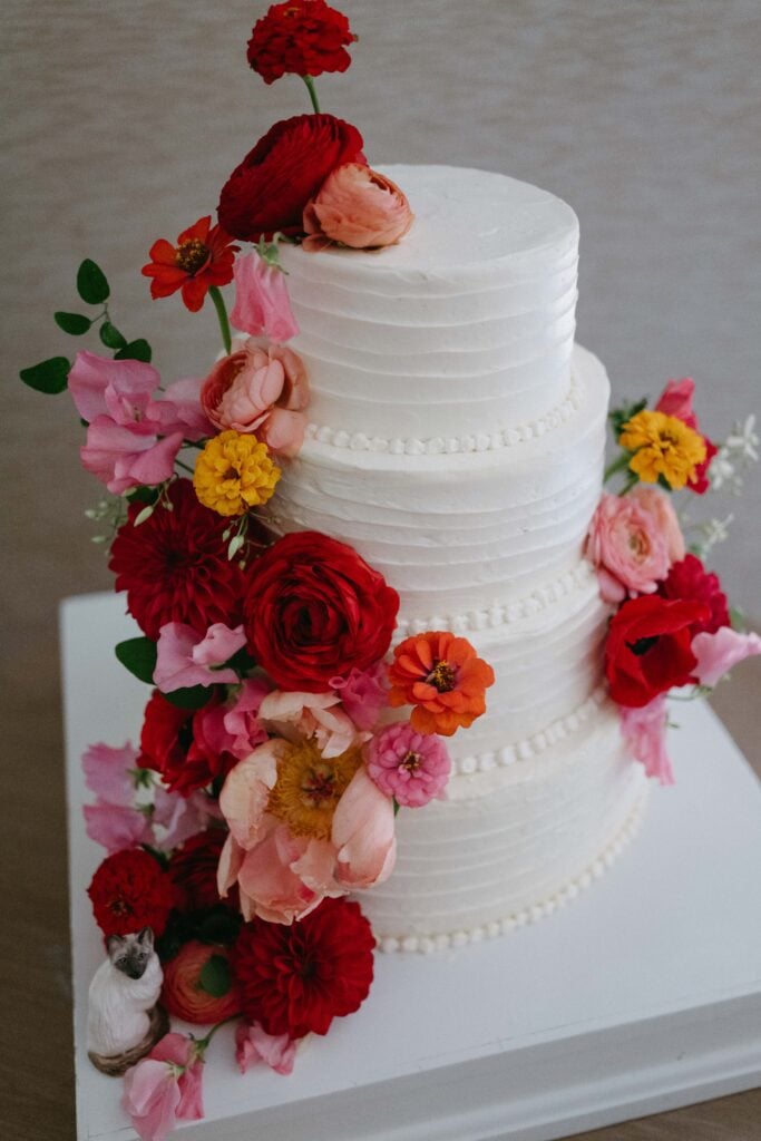 White tiered wedding cake with pink yellow and red florals