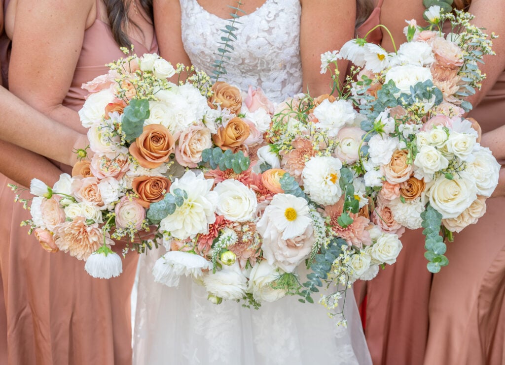 Bridesmaids and bride in peach dresses holding white and orange bouquets