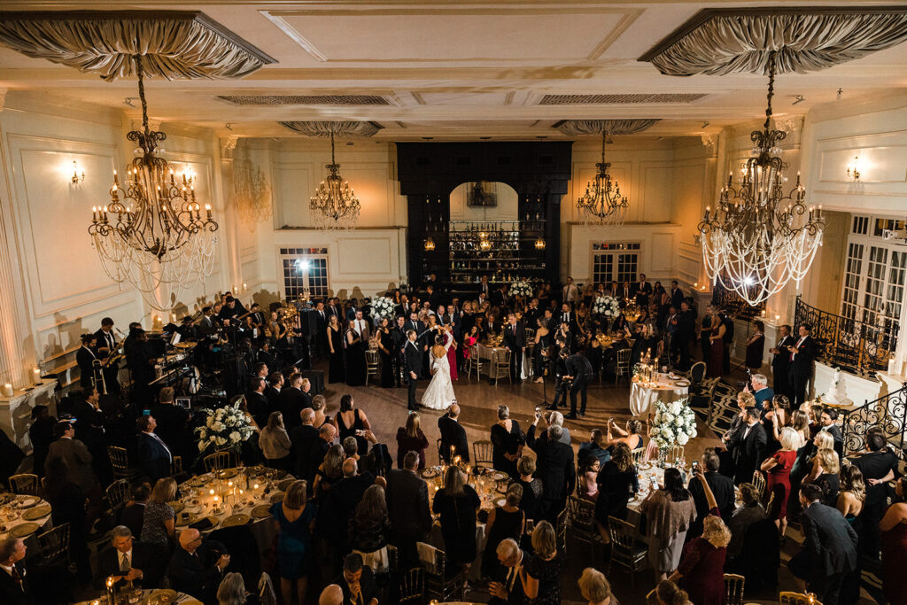 Bride and groom dancing on ballroom floor at wedding reception while guests watch.