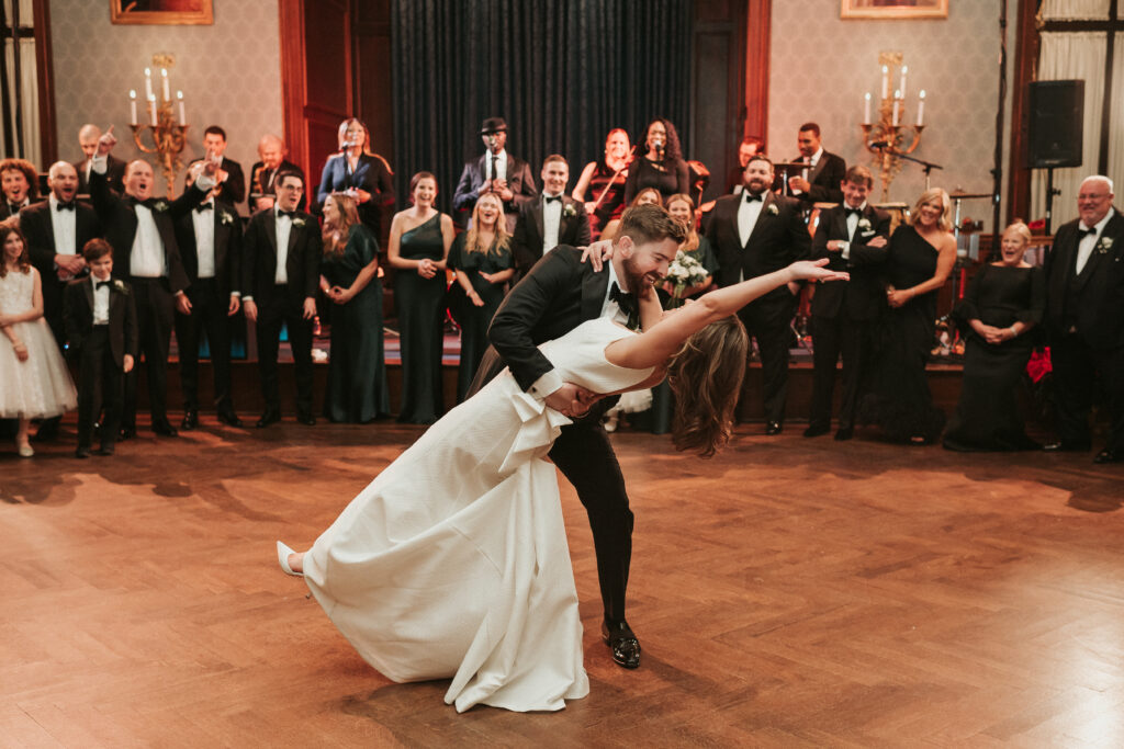 Groom dips his bride on the dance floor at the Philadelphia Union League as Jellyroll plays a song and guests look on.